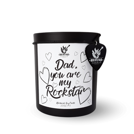 Schwarzes Kerzenglas mit Aufschrift Dad you are my Rockstar und Gitarrenplektrum mit Rockstar Candle Logo als Dekoration.