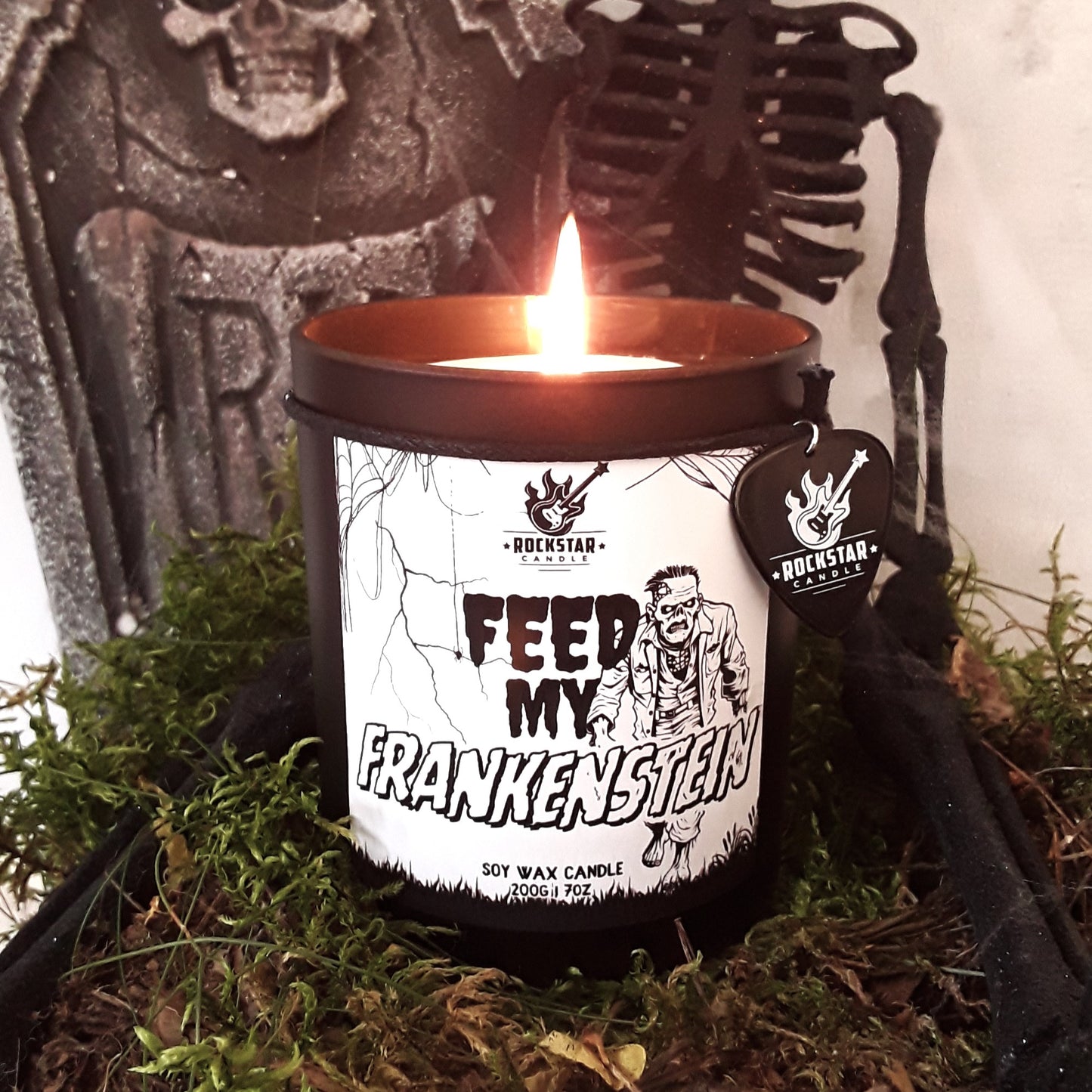 Schwarze Kerze mit weißer Aufschrift Feed my Frankenstein und Frankenstein-Figur, im Hintergrund Halloween Dekoration