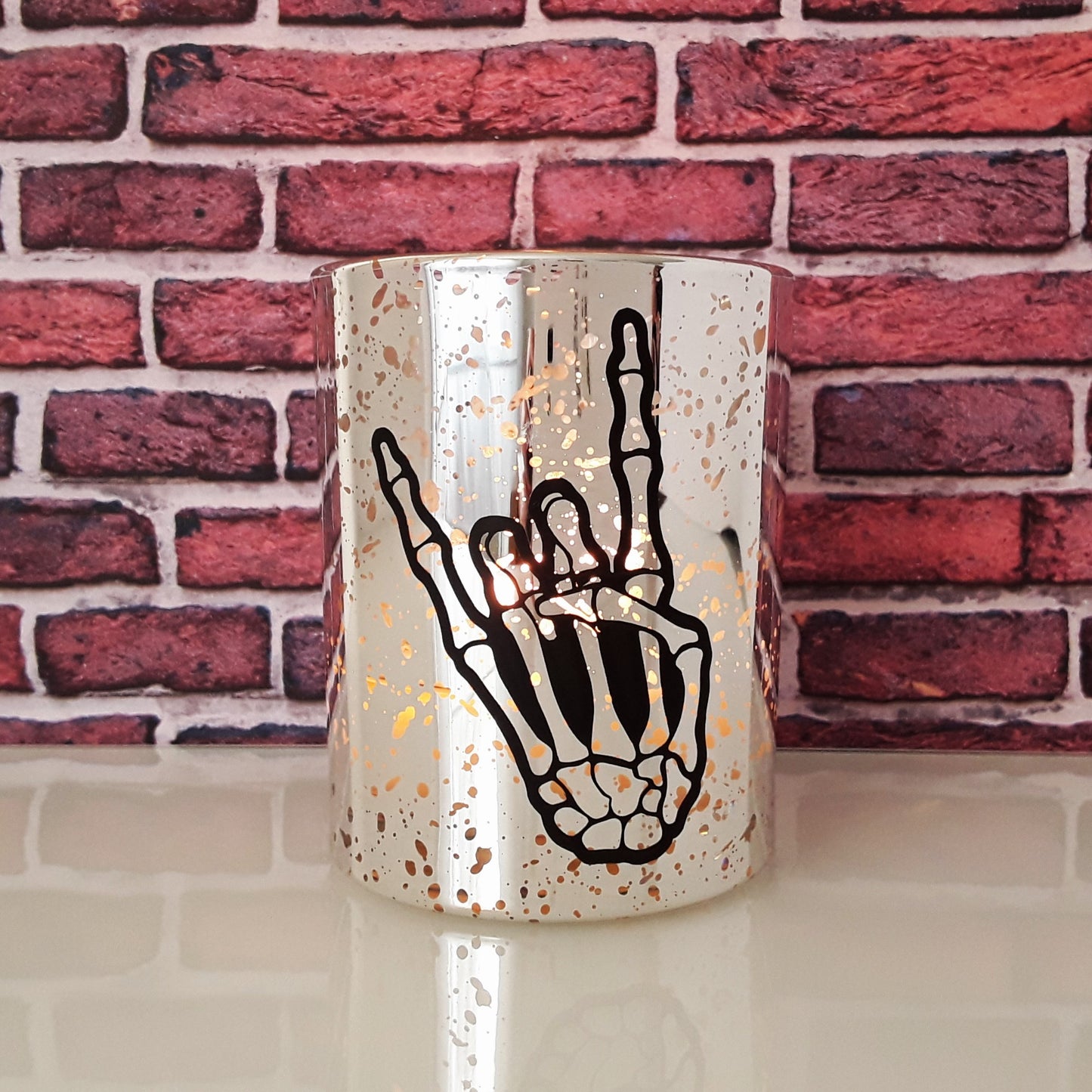 Kerze silber Skeletthand brennend vor Backsteinwand