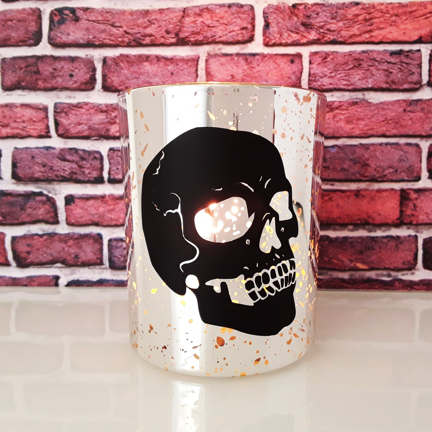 Kerze silber Schädel brennend vor Backsteinwand