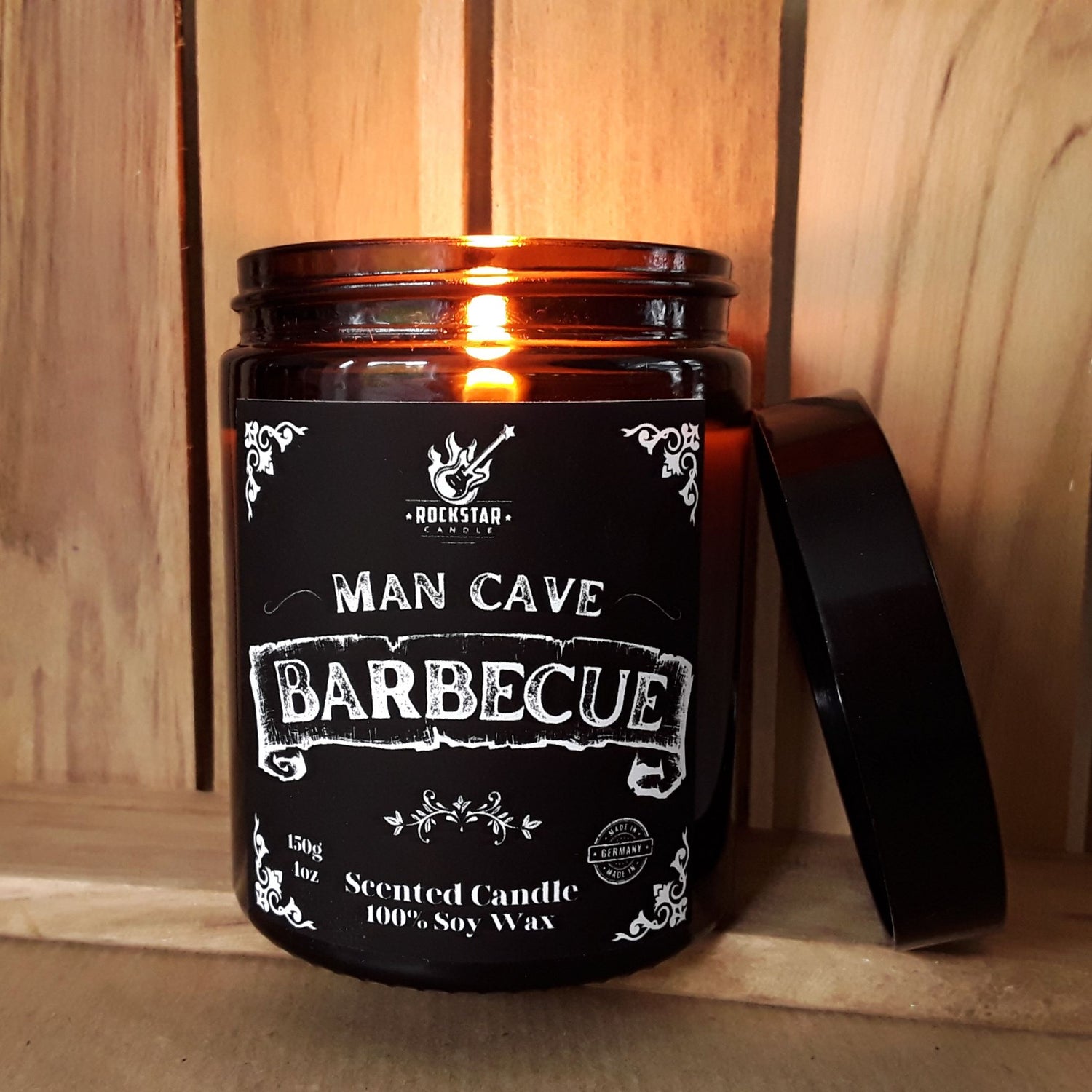Brennende Kerze in braunem Glas mit Deckel, schwarzes Etikett mit weißer Beschriftung Barbecue